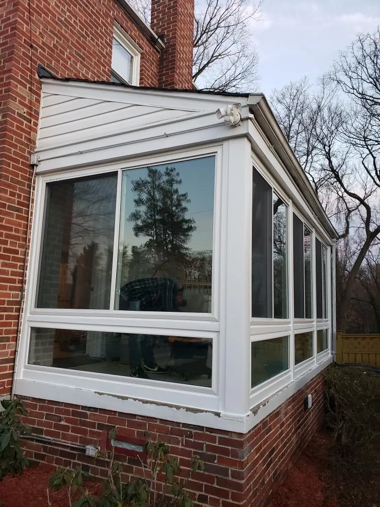 A glass-walled three-season sunroom enclosure glazed onto a red brick house