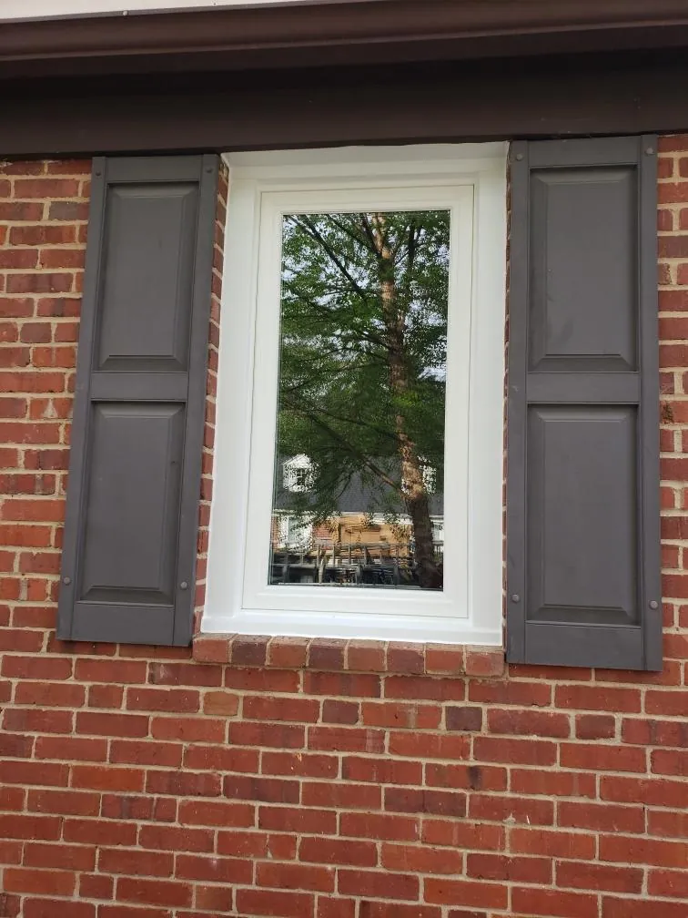 Single casement window in red brick flanked by grey shutters